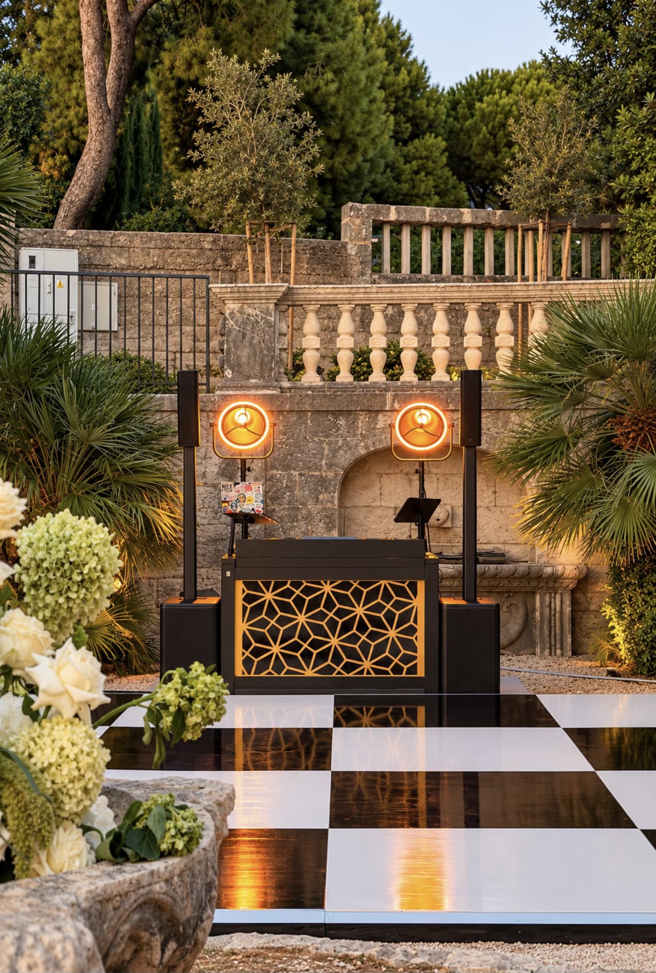 Luca Goya’s complete outdoor DJ setup with a black booth, illuminated geometric front, two speakers and warm circular lights beside a dance floor